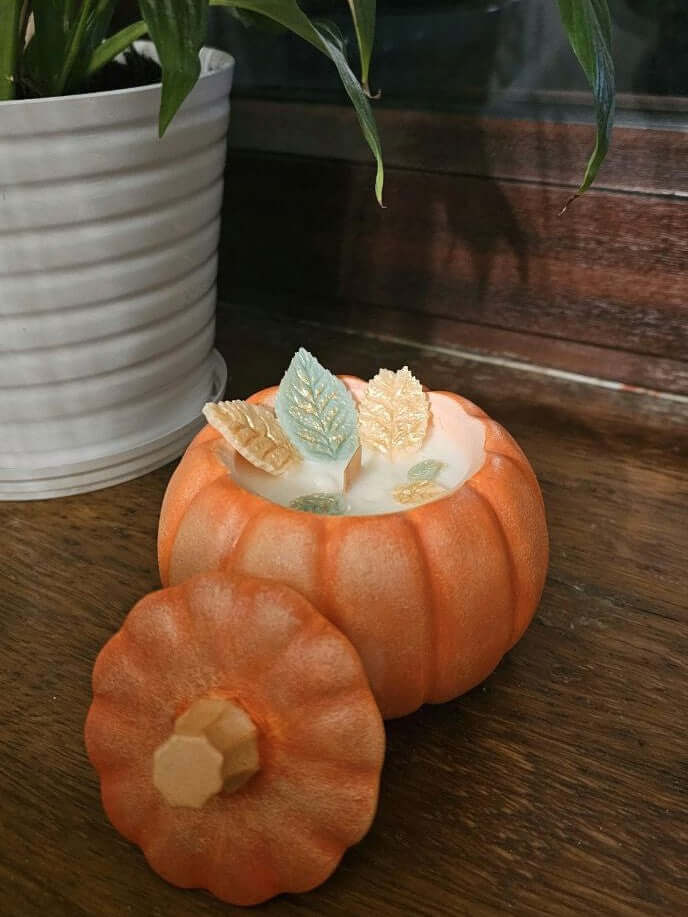 Pumpkin soy candle with wooden wick in pumpkin shape, featuring leaf decorations, ideal for autumn decor.